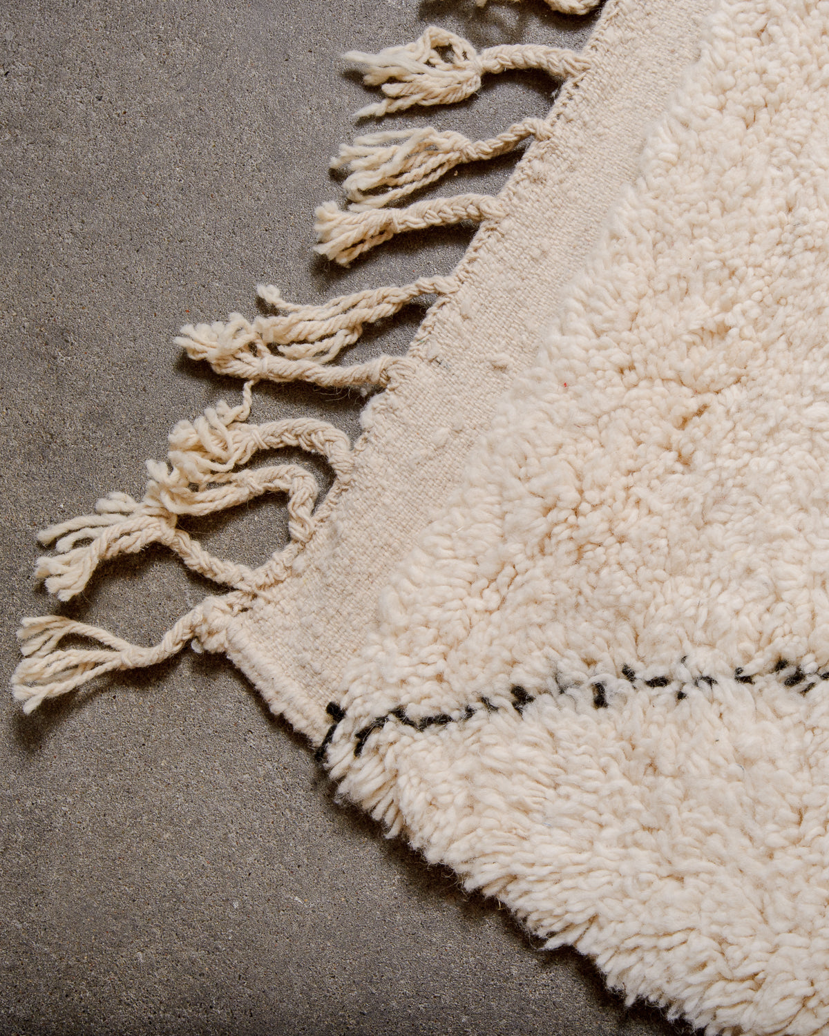 Natural wool tassels on edge of Berber rug with black and white details.